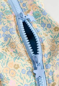 Floral-patterned fabric with pastel colors, featuring a blue zipper with a star-shaped pull tab. Close-up of zipper detail and texture.