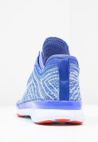 Zapatilla deportiva azul con un upper de punto texturizado y un diseño estampado, tirador en el talón y una suela blanca con acentos rojos.