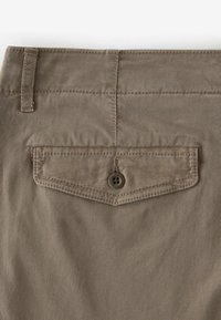 Pantaloni in cotone color khaki con una tasca posteriore dotata di chiusura a bottone. Il tessuto ha una finitura testurizzata con sottili linee orizzontali.