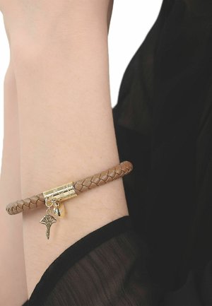 Pols met een gevlochten bruin leren armband met een gouden sluiting en twee gouden bedels, één in de vorm van een waaier en de andere een afgeronde tag.