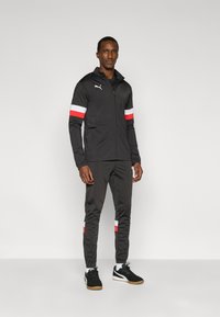 Μαύρη αθλητική φόρμα με ζακέτα με φερμουάρ και κόκκινες και λευκές ρίγες στα μανίκια, σετ με παντελόνι που ταιριάζει.