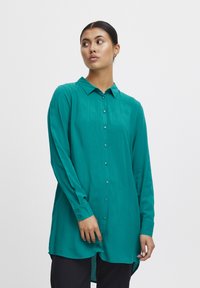 Teal long-sleeve shirt with a button front, collar, and side slits. Made from a smooth, lightweight fabric with a soft texture.