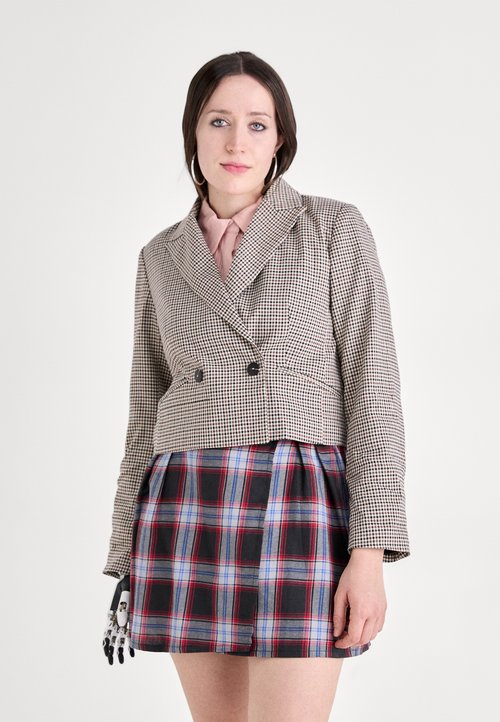 Kurzer Hahnentritt-Blazer mit zwei schwarzen Knöpfen, kombiniert mit einem gefalteten Karorock in rot, blau und schwarz.