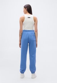 Ανοιχτό μπλε φόρμας με ελαστικά μανσέτες και πίσω τσέπη, συνδυασμένο με εφαρμοστή λευκή αμάνικη μπλούζα με μικρή ετικέτα λογότυπου.