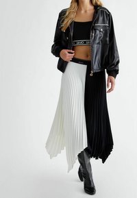 Gonna midi plissettata bianca e nera con orlo svasato, abbinata a una giacca bomber in satin nero e stivali neri testurizzati al ginocchio.