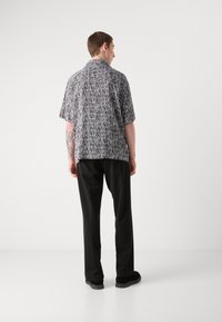 Short-sleeve shirt in black and white abstract pattern, paired with black trousers and shoes, viewed from the back against a plain background.