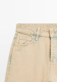 Jeans in denim beige con un motivo blu sbiadito. Presentano una tasca frontale, chiusura con bottone e cuciture robuste. Texture liscia con una leggera lucentezza.