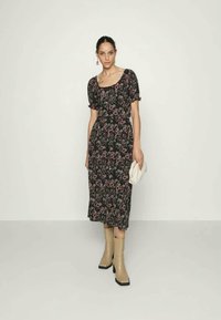 Vestido midi preto com estampado floral e mangas bufantes, apresentando padrões em rosa e verde. Usado com botas de cano alto bege e segurando uma clutch branca.