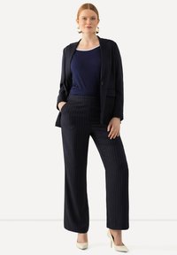 Marinblå randig kostym bestående av en strukturerad kavaj och vida byxor, i kombination med en figursydd marinblå topp och ljusa klackar.
