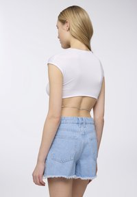Top corto bianco con maniche corte, abbinato a pantaloni corti in denim azzurro chiaro con orlo sfilacciato e due tasche posteriori. Accentatura a catena in vita.