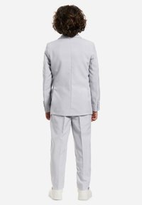 Completo grigio chiaro con blazer strutturato e pantaloni coordinati, caratterizzato da un design pulito e sartoriale. Abbinato a sneakers bianche.