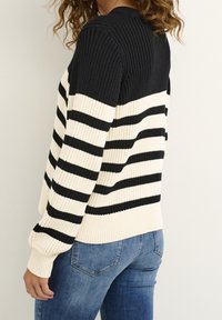 Svart och krämrandig tröja med ribbad textur, med långa ärmar och rund halsringning, tillsammans med blå denimjeans.