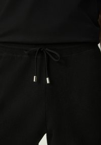 Schwarze Jogginghose mit weicher Textur, ausgestattet mit einem figurbetonten Bund, verstellbarem Kordelzug mit metallischen Enden und einem schlichten Design.