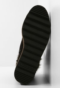 Semelle en caoutchouc noir avec texture striée. Présente un accent en fausse fourrure sur les côtés. Taille 37 visible sur la semelle.