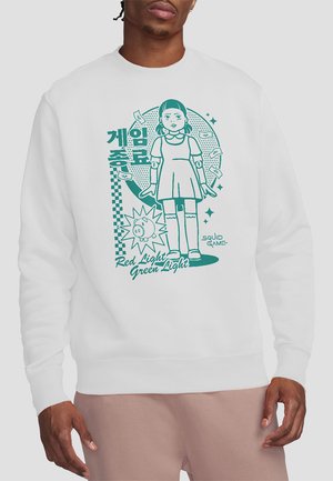 Weißer Pullover mit grünem Grafikdesign eines Mädchens in einem Kleid und dem Text "Red Light Green Light" sowie elementen, die mit einem Spielthema verbunden sind.