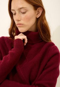 Suéter burdeos de cuello alto hecho de suave lana, con puños acanalados, patrón texturizado y un ajuste relajado, visto en un primer plano del escote.
