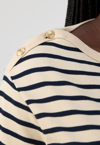 Striped T-shirt in cream and navy, featuring two gold button accents on the shoulder, soft texture, and a relaxed fit design.
