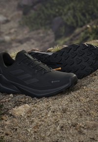 Czarne buty trekkingowe Gore-Tex z teksturowaną podeszwą, wypoczywające na skalistym terenie na zewnątrz.
