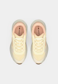 Lacoste sneakers with a light yellow mesh and leather upper, cream accents, and a peach lining. Features flat laces and a rubber sole.