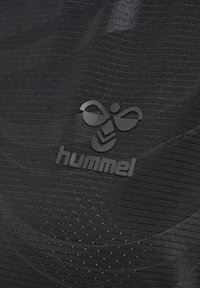 Il tessuto atletico nero presenta una superficie strutturata con costine orizzontali. Il logo "hummel" è ben visibile in finitura nera opaca.