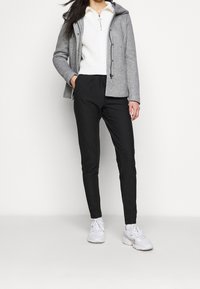 Šedá mikina na zip, bílý svetr s pleteným vzorem a černé pruhované kalhoty s tapered střihem; nošeny s bílými teniskami. Jednoduchý, funkční outfit.