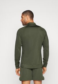 Mørkegrønn langermet treningsgenser med høy krage, tettsittende design, flatlocksømmer og en glatt tekstur, sammen med matchende shortser.