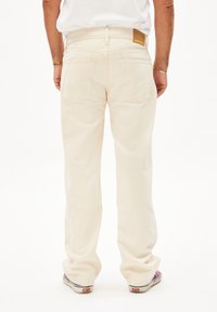 Lichtbeige jeans met een losse fit, voorzien van twee achterzakken en een bruine leren patch op de tailleband. Glad stoftextuur.
