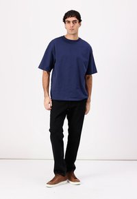 Tricou din bumbac de culoare albastru marin, cu o croială lejeră, mâneci scurte și guler rotund; purtat cu blugi negri și teniși maro. Textură simplă și netedă.