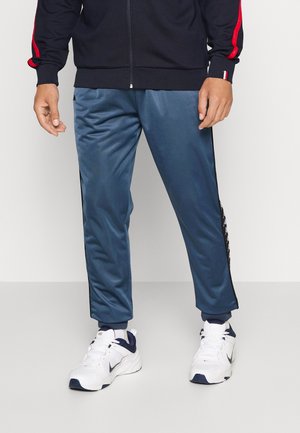 Blauwe satijnen trainingsbroek met een slim fit, voorzien van zijstrepen en elastische boorden, gecombineerd met witte sneakers.