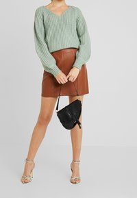 Ljust grönt stickat tröja med V-hals, tillsammans med en brun läder minikjol. Svart handväska i krokodilmönster och silverfärgade skor med remmar.