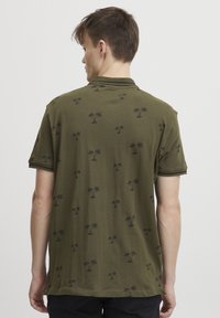 Grønn polo skjorte med et mønster av små svarte palmer, korte ermer og krage med aksentstriper. Mykt bomullsstoff.