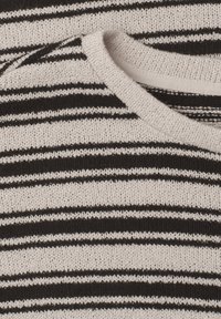Gros plan d'un pull tricoté beige avec des rayures noires horizontales irrégulières et un col rond.