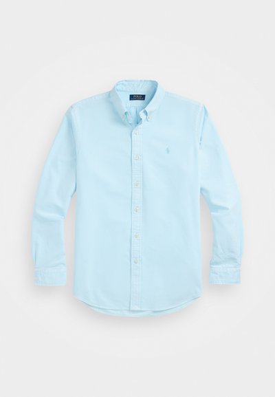 Ανοιχτό μπλε πουκάμισο με γιακά φτιαγμένο από βαμβάκι, διαθέτει μακριές μανσέτες, κουμπιά μπροστά και ένα μικρό λογότυπο στην αριστερή πλευρά του στήθους.