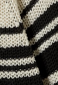 Tessuto lavorato a maglia con strisce alternate di nero e crema. La texture è a trama aperta e leggera, con un design morbido.