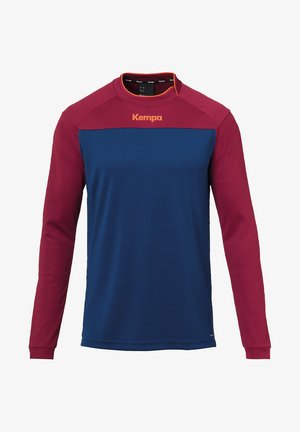 Langærmet skjorte i rød og blå. Blødt stof med kontrasterende ærmer. Rund hals med orange accenter. Har "Kempa"-logoet på brystet.
