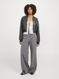 Svart cropped leather bomberjakke over en hvit bluse med broderi, parret med høytlivs grå vide jeans og svarte spisse sko.