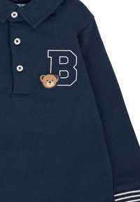 Polo di colore blu navy in cotone, con una "B" bianca e un'emblema di un orso sul petto sinistro, completo di dettagli a righe sulle maniche.