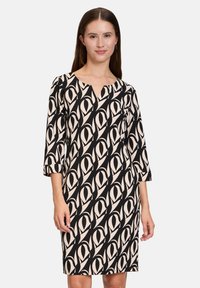 Schwarz-beiges gemustertes Kleid mit drei Viertelärmeln, V-Ausschnitt und lockerem Schnitt, das ein geometrisches Augendesign aufweist.