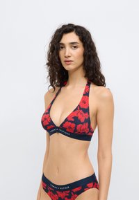 Τριγωνικό τοπ μπικίνι σε ναυτικό μπλε με κόκκινο λουλουδάτο μοτίβο και λουρί με λογότυπο. Λείος υφής, σχέδιο με λαιμόκοψη halter, σετ με ταιριαστά σλιπ.