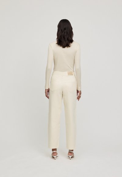 Maglietta a maniche lunghe a righe crema abbinata a pantaloni a gamba dritta crema a vita alta, con un design della tasca posteriore e hardware di colore chiaro.