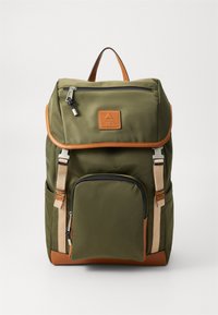 Sac à dos vert olive en tissu avec un fond en cuir marron, comprenant une poche avant, un rabat supérieur, des bretelles réglables et des accents métalliques.