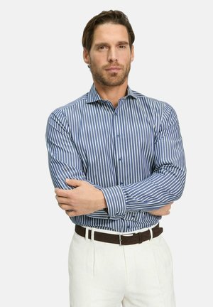 Blau-weiß gestreifte Button-up-Bluse mit langen Ärmeln, kombiniert mit weißen Hosen und einem braunen Gürtel, der eine taillierte Passform aufweist.