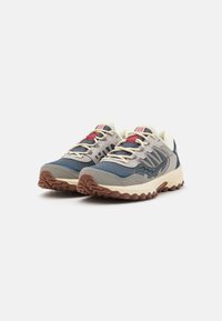 Chaussures de trail pour hommes avec un dessus en mesh gris, accents bleus, semelle beige, lacets rouges et semelle extérieure en caoutchouc texturé pour une meilleure adhérence.