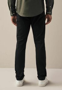 Schwarze Hosen aus weichem Stoff, mit einer schmalen Passform, geraden Beinen und einer glatten Textur, kombiniert mit weißen Sneakers.