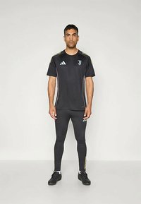 T-shirt de sport noir et leggings avec des accents jaune et bleu clair. Présente le logo Adidas et l'emblème de la Juventus. Fabriqué en matériau respirant.