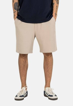 Pantalones cortos beige y texturizados con bolsillos laterales, de largo hasta medio muslo, combinados con zapatillas azul marino y blancas con acentos a rayas.