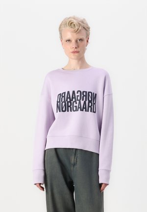 Svetlo fialový skrátený sveter s čiernym grafickým nápisom "NORGAARD" vytlačeným na prednej strane. Má dlhé rukávy a voľný strih.