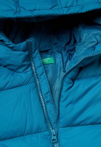 Tyrkysová péřová bunda s předním zipem, prošívaným vzorem a vnitřním podšívkou. Obsahuje zelenou značka, která je viditelná uvnitř.