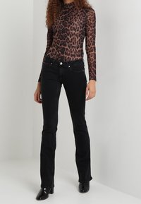 Bluzka z długim rękawem w panterkę z przezroczystego materiału, w połączeniu z dopasowanymi czarnymi dżinsami i czarnymi szpilkami.