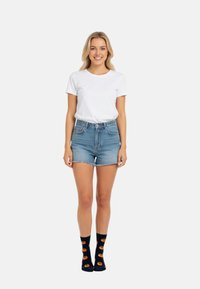 Biała bawełniana koszulka, jasnoniebieskie dżinsowe szorty z postrzępionym wykończeniem oraz ciemnoniebieskie skarpetki z pomarańczowymi wzorami donutów. Czysty design, swobodny krój.